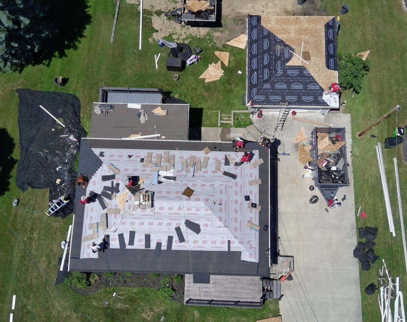 Aerial view of a house roof under construction with workers, tools, and scaffolding in a yard