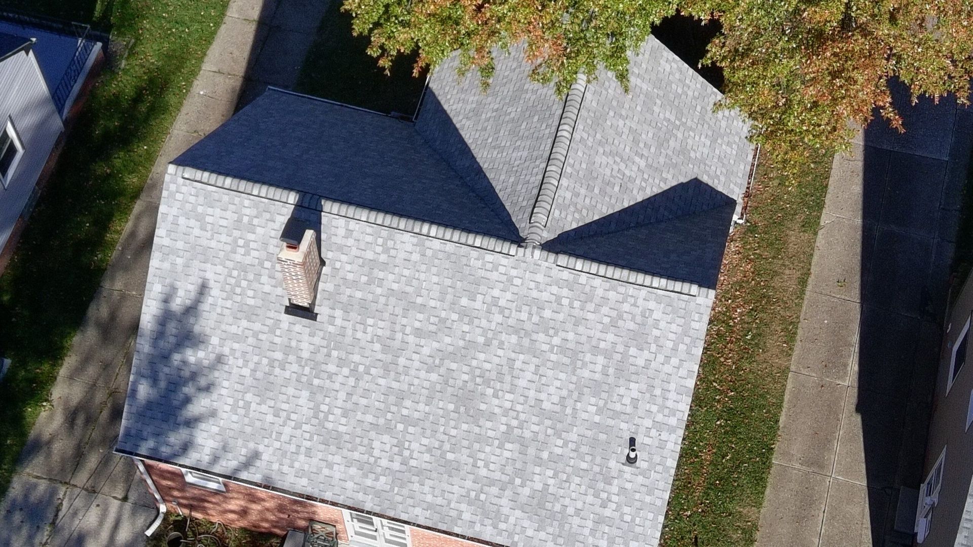 Aerial view of a gray-roofed house with a chimney, surrounded by trees and a driveway.