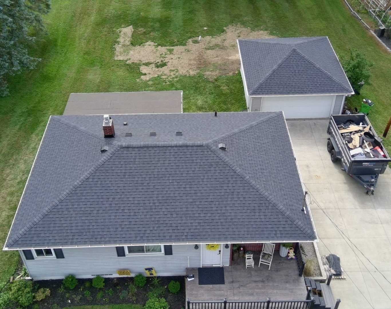 Aerial view of a suburban house with gray roof, driveway, detached garage, and a truck parked beside it.