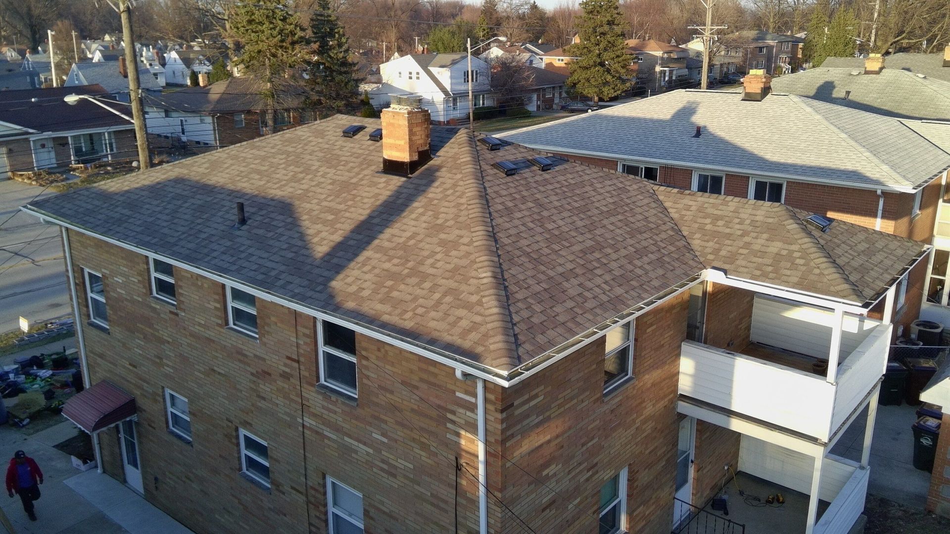 Aerial view of a brown brick house with a new shingled roof and neighboring homes in a residential area.