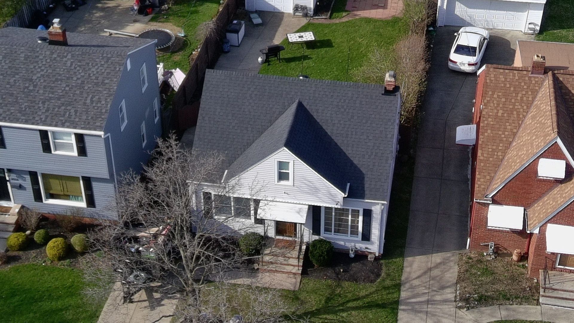 Aerial view of a small white house with a dark roof between two neighboring homes.