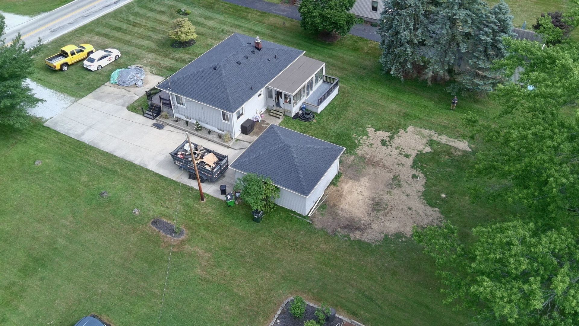 Aerial view of a suburban house with a driveway, detached garage, and lawn with a bare dirt patch.