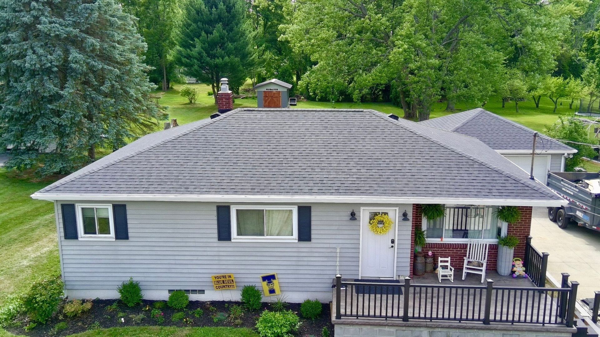 Gray house with a small front porch, white trim, and trees and greenery in the yard.