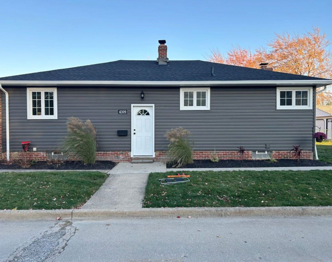 Gray single-story house with white trim, front door, walkway, and small lawn by the street.
