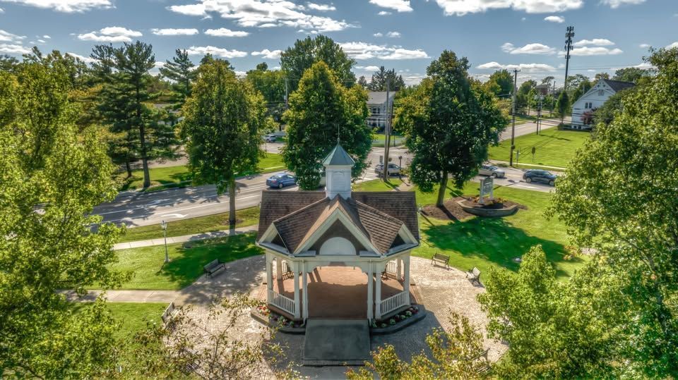 Small gazebo in a sunny park with trees, grass, and a road in the background