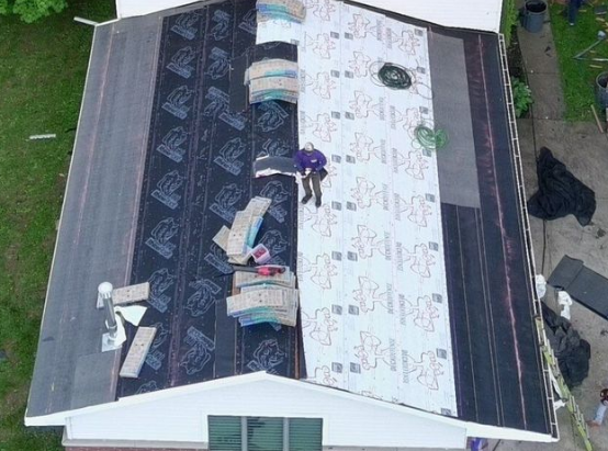 Damaged roof being repaired, with workers and construction materials on a white house.
