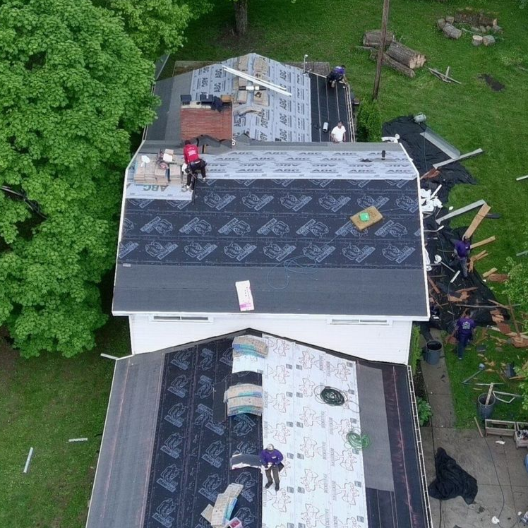 Aerial view of roofers repairing a house roof beside a large green tree in Macedonia, Ohio