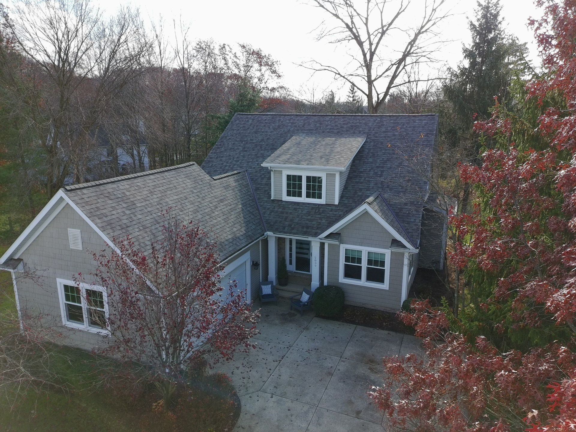 Aerial view of a gray house with white trim, surrounded by leafless trees and a red tree in front.