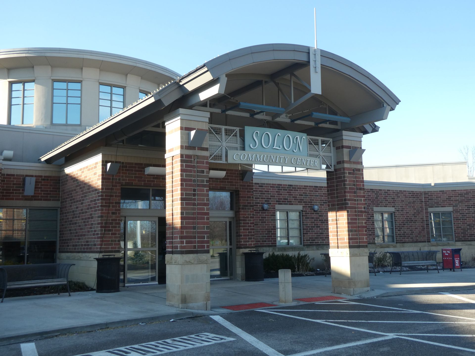 Brick building entrance with covered awning and “SOC C” sign, viewed from a parking lot.