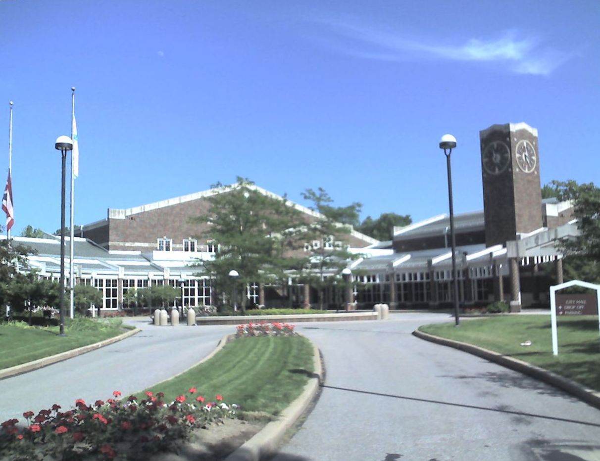 Hospital entrance drive with landscaped flower beds and a brick tower on a sunny day