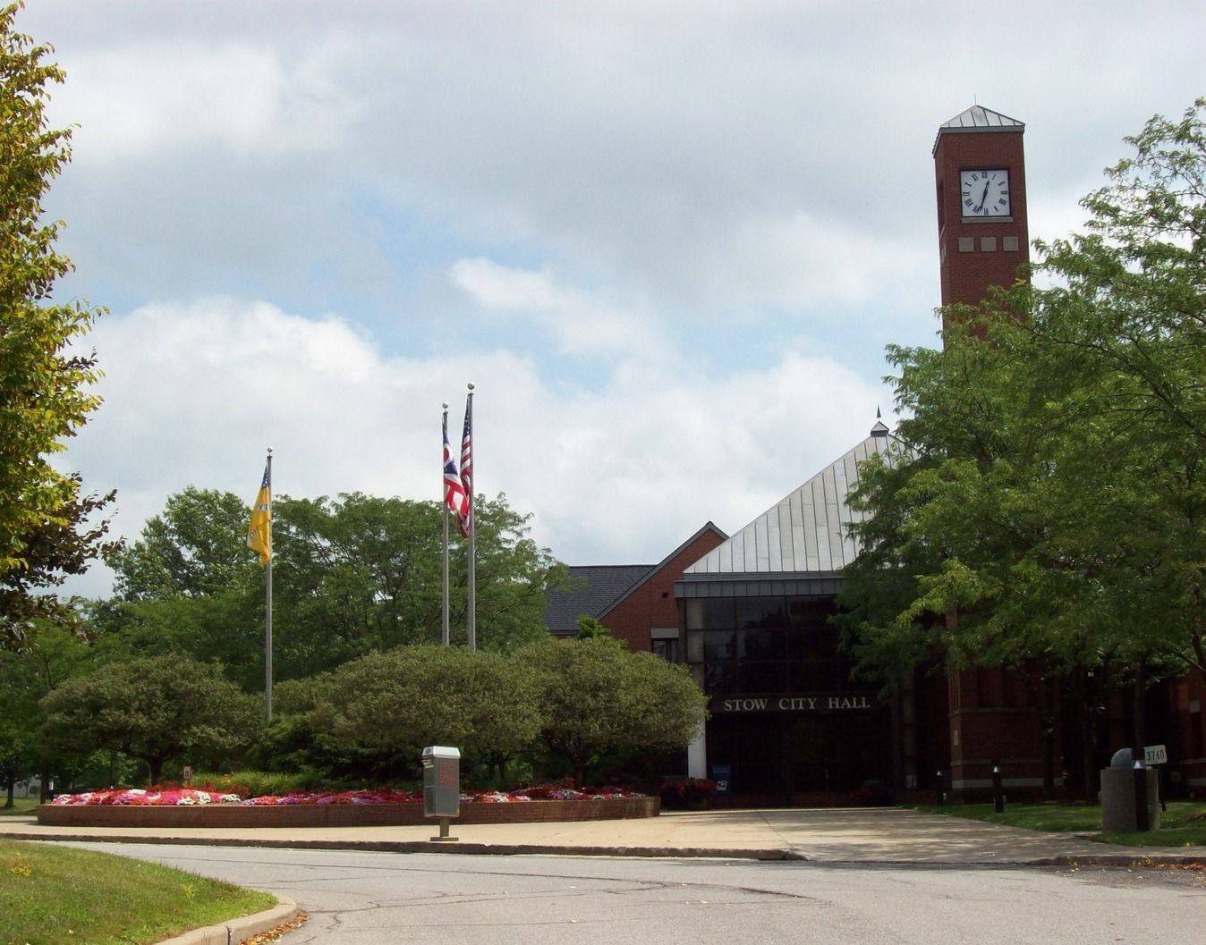 Campus entrance with flagpoles, trees, and a clock tower under a cloudy sky