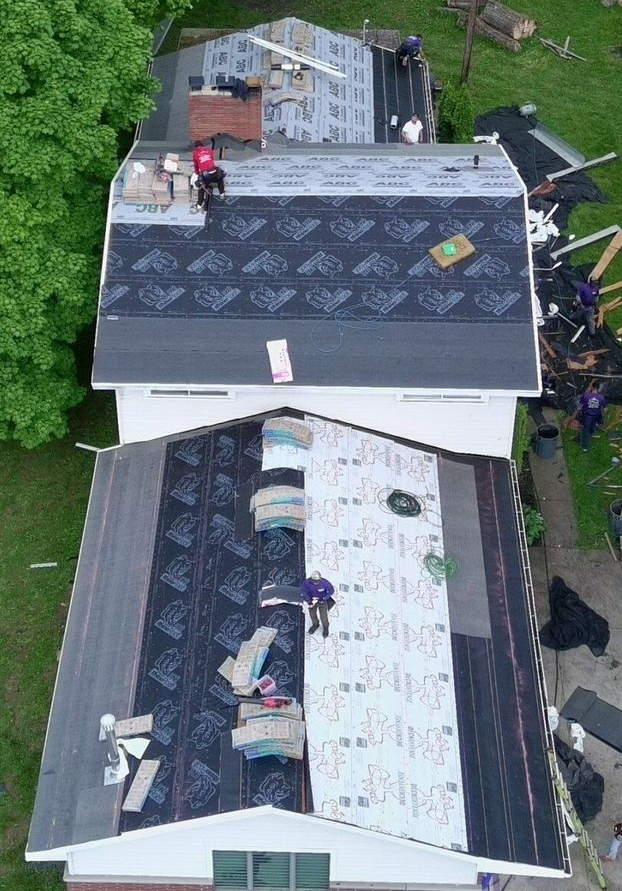 Aerial view of roofers repairing a shingled house roof in Twinsburg 
with dark and white roofing materials