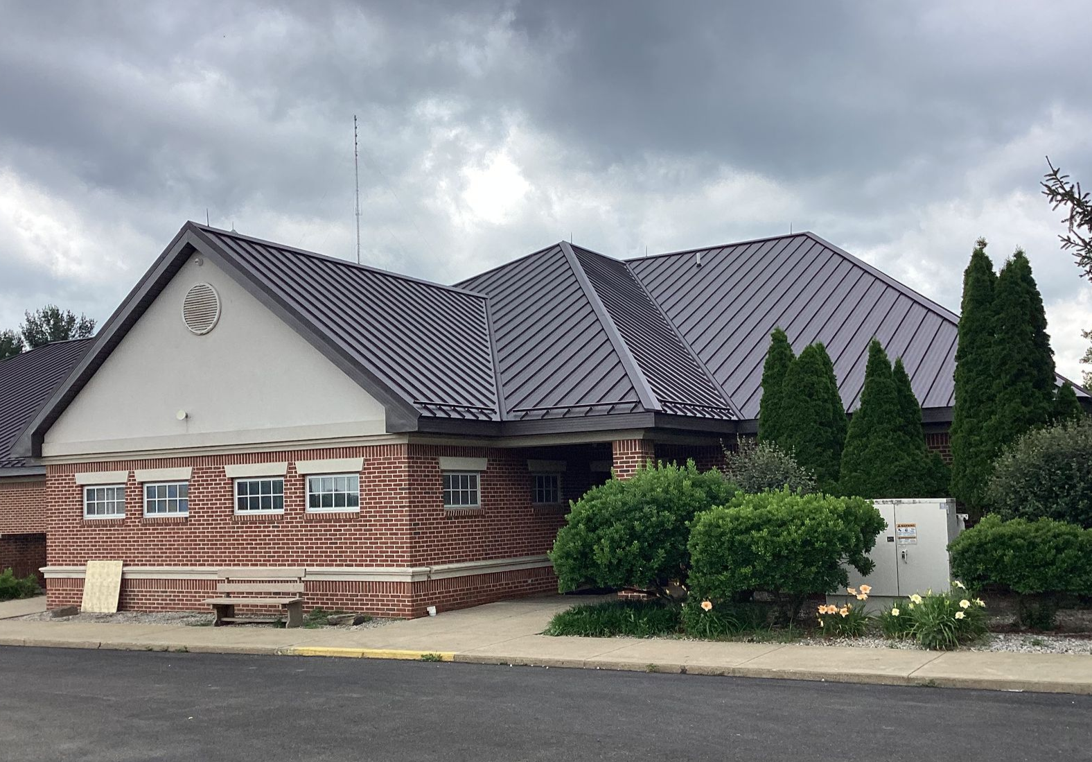 Brick building with dark gray roof, trimmed hedges, and cloudy sky