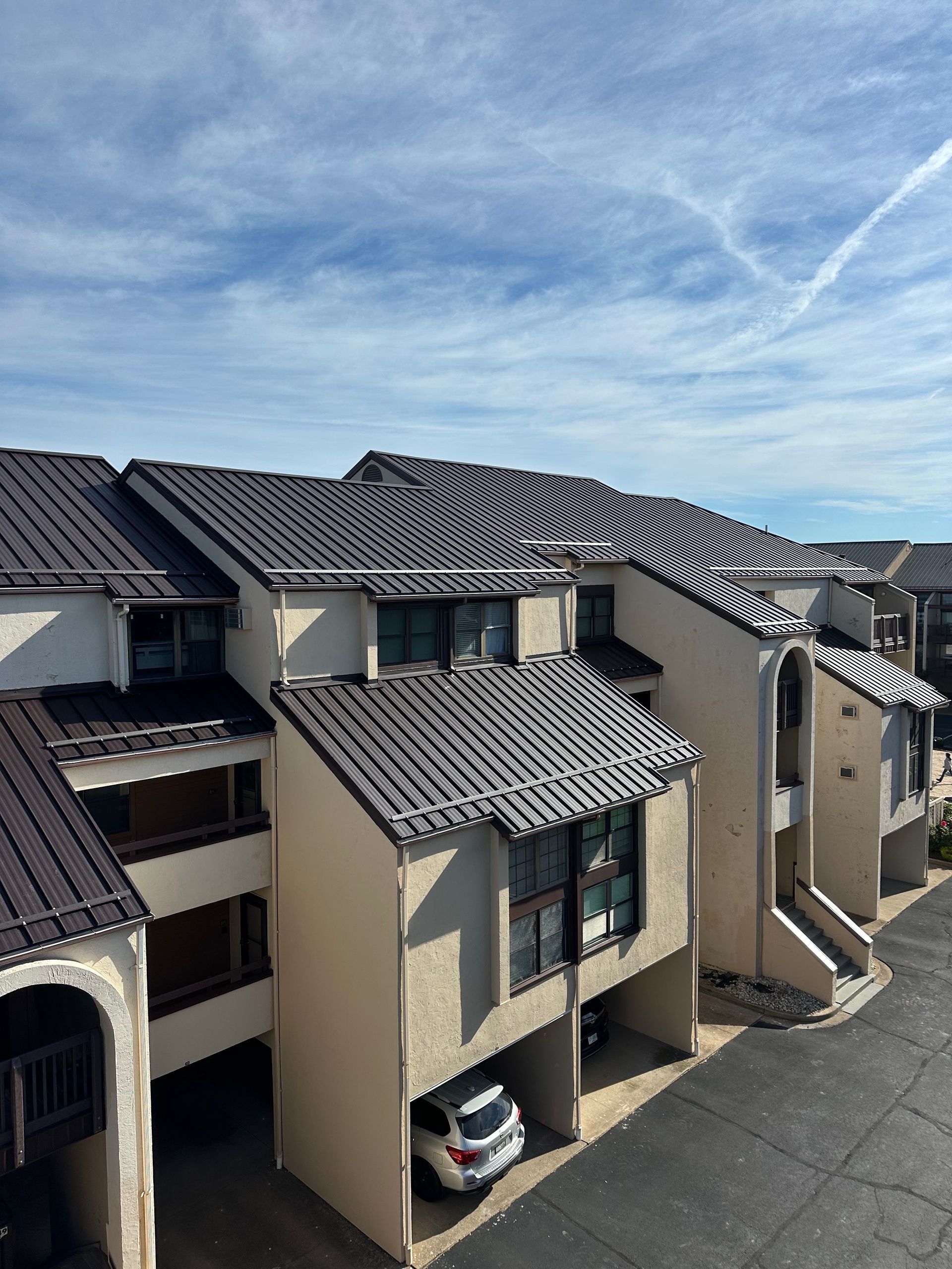 Row of beige townhouses with dark tiled roofs and a parked car under a bright blue sky