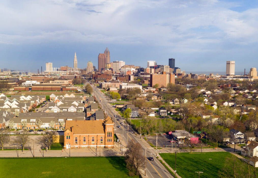Aerial view of a city skyline over neighborhoods, roads, and a green park under a partly cloudy sky