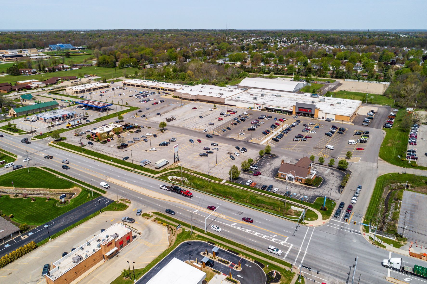 Aerial view of a large shopping center parking lot with multiple stores and roads nearby