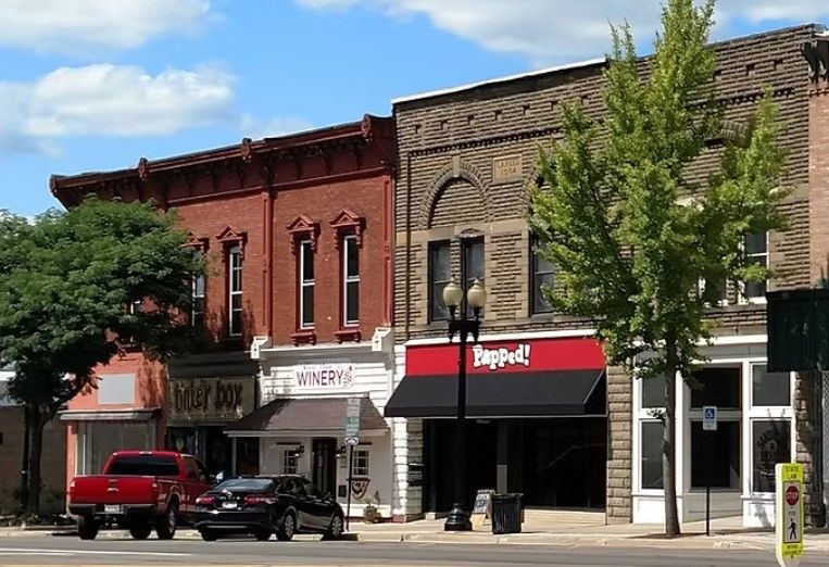 A street-level view of a line of historic brick storefronts with a red pickup truck and black sedan parked in front.