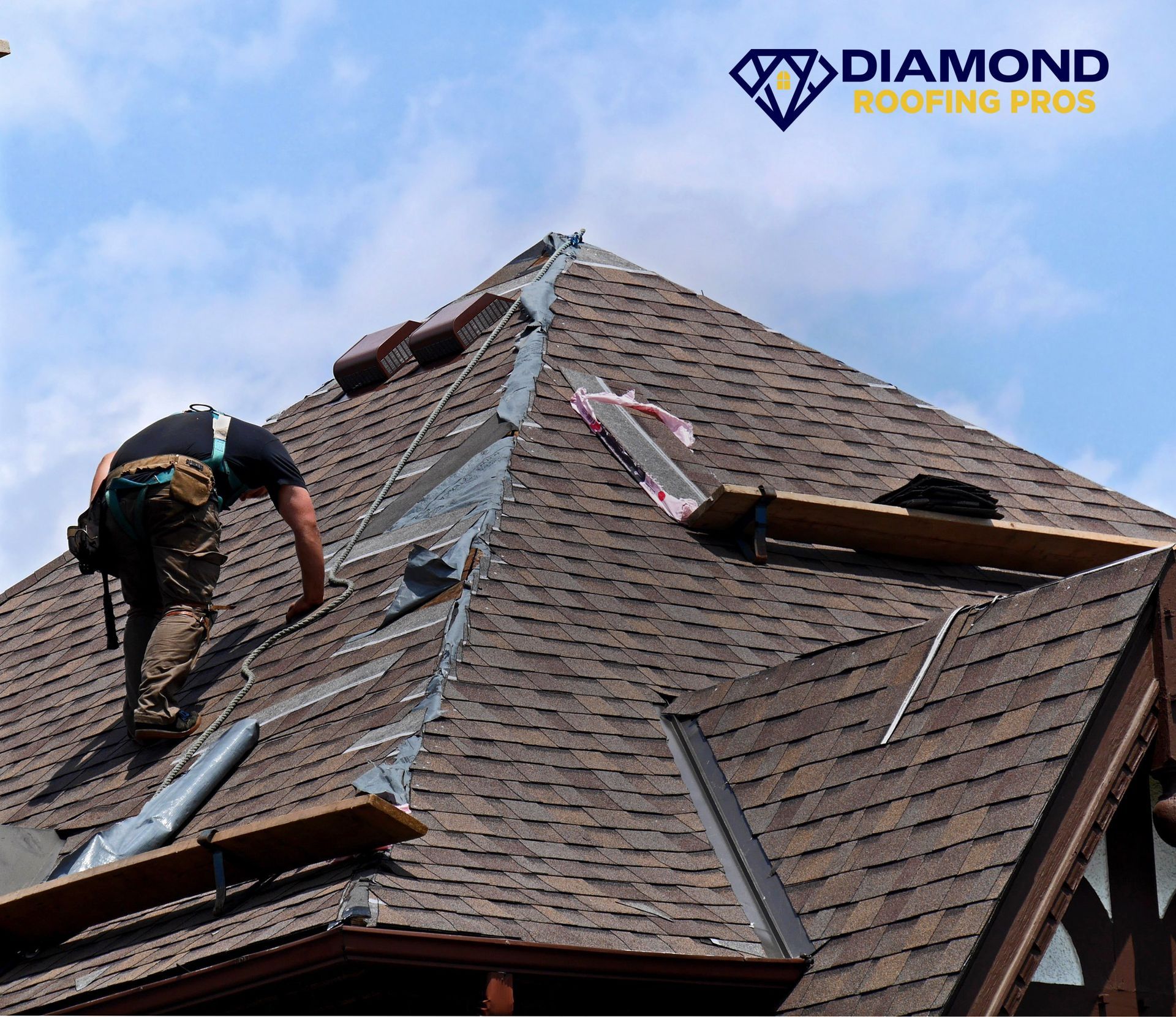 Roofer working on a steep shingled roof under a blue sky, with Diamond Roofing Pros logo visible