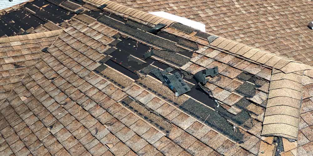 Damaged shingled roof with missing and torn tiles exposing the underlayment
