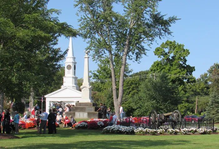 White church with steeple and crowd outdoors in a green park on a sunny day
