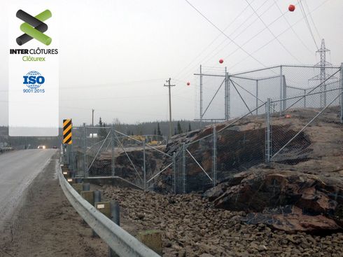 Travaux de voirie en bordure de route le long d'une voie ferrée clôturée, terrain endommagé et poteaux électriques en construction.