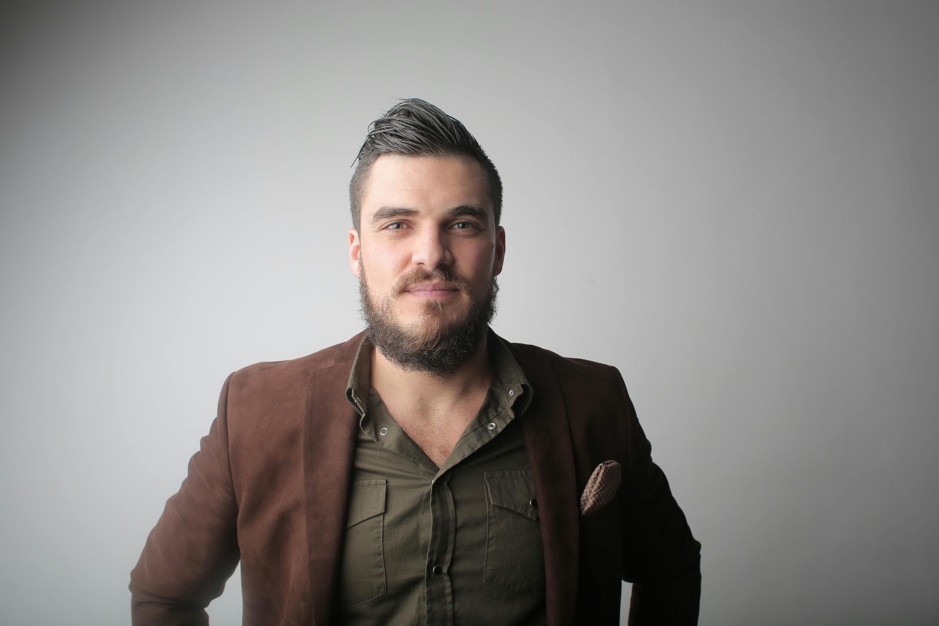 Portrait of a man with a beard in a brown jacket against a gray background