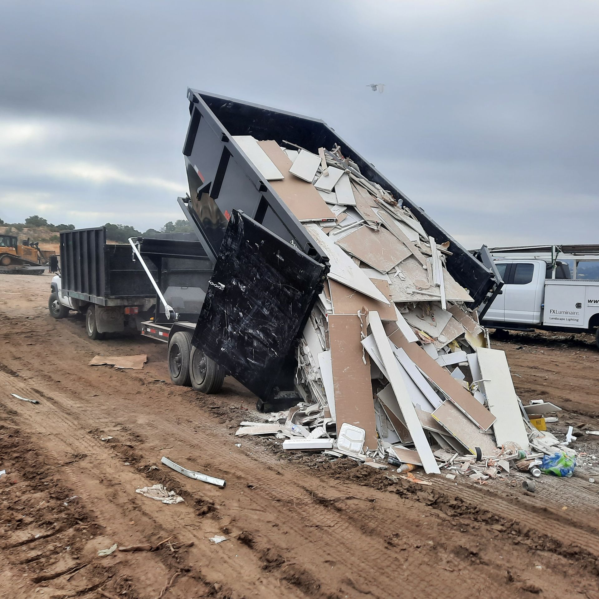 Dump truck dumping construction debris onto muddy ground.