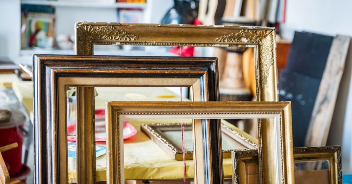 Ornate gold and brown wood frames are positioned against a table. Pieces of art are on the wall and 