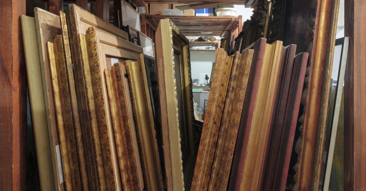 A row of numerous ornate wooden frames are positioned upright on a large shelf located in a storage space.