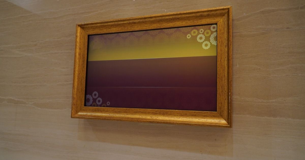A burgundy and yellow abstract piece of art is framed by a thick gold wooden frame. The art is mounted on a wall.