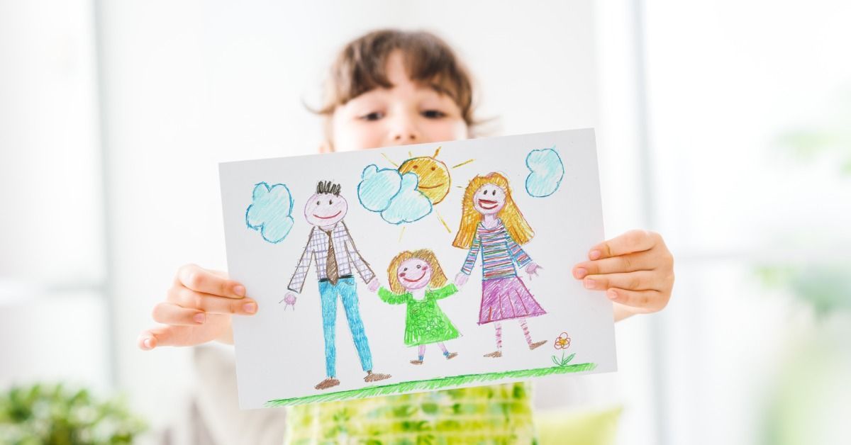 A young girl holding a colorful crayon drawing of three smiling people beneath blue clouds and a yellow sun.