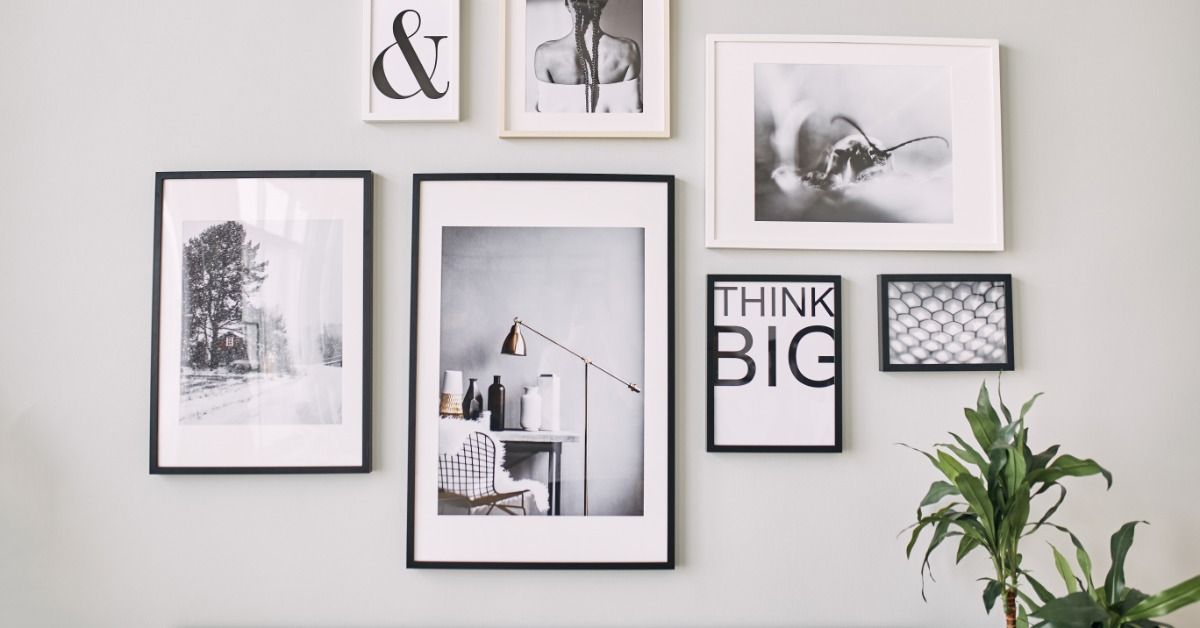 Black and white posters of varying sizes are in neutral-colored frames with white mats. They're arranged on a wall.