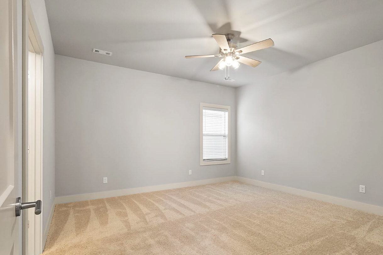 Empty bedroom with tan carpet, light gray walls, and a ceiling fan.
