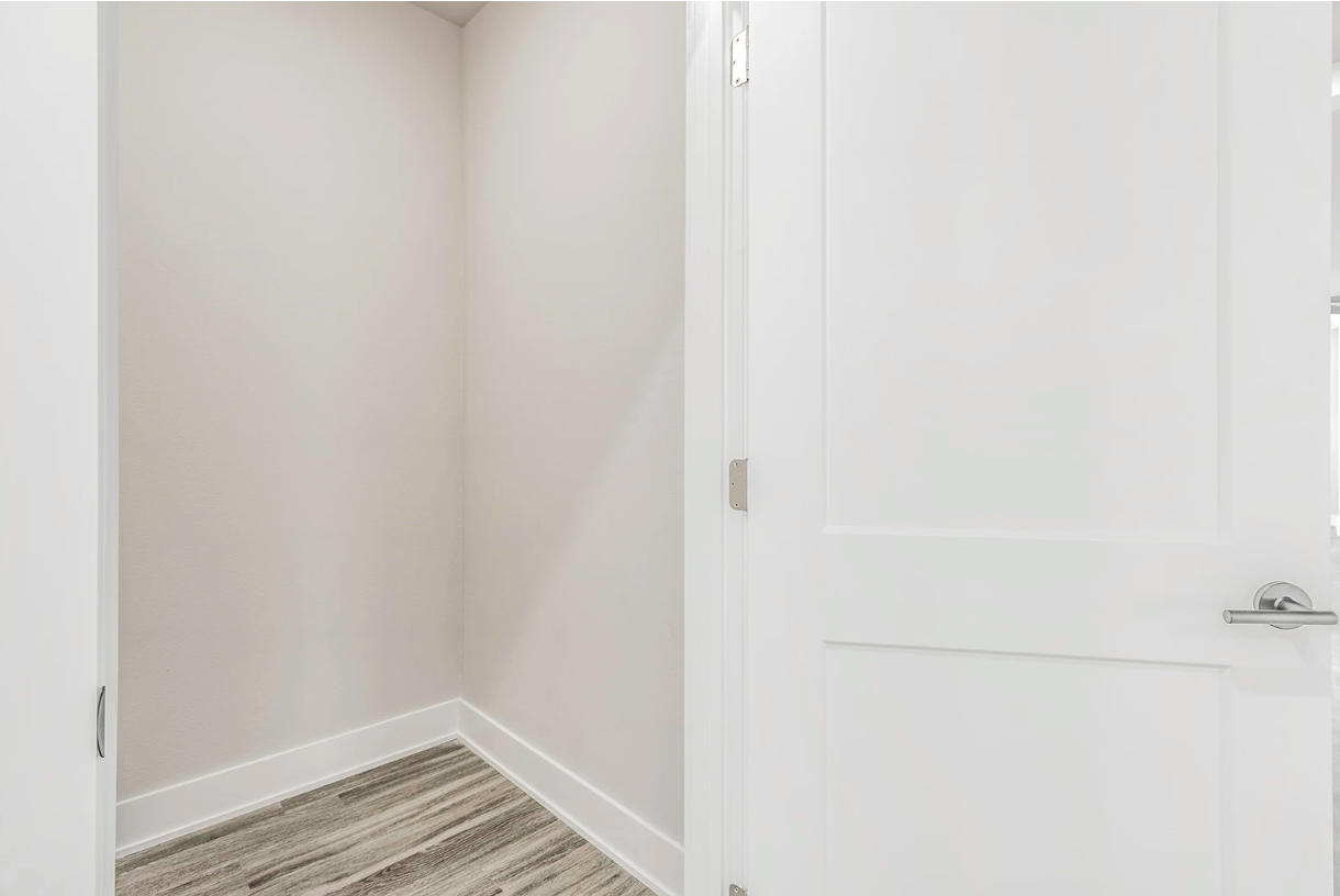 A white door opens to a small closet with pale walls and a patterned floor.