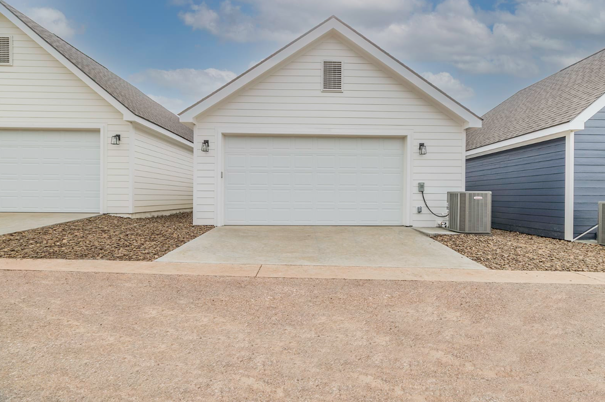 White detached garage with a concrete driveway, flanked by other garages, gravel ground.