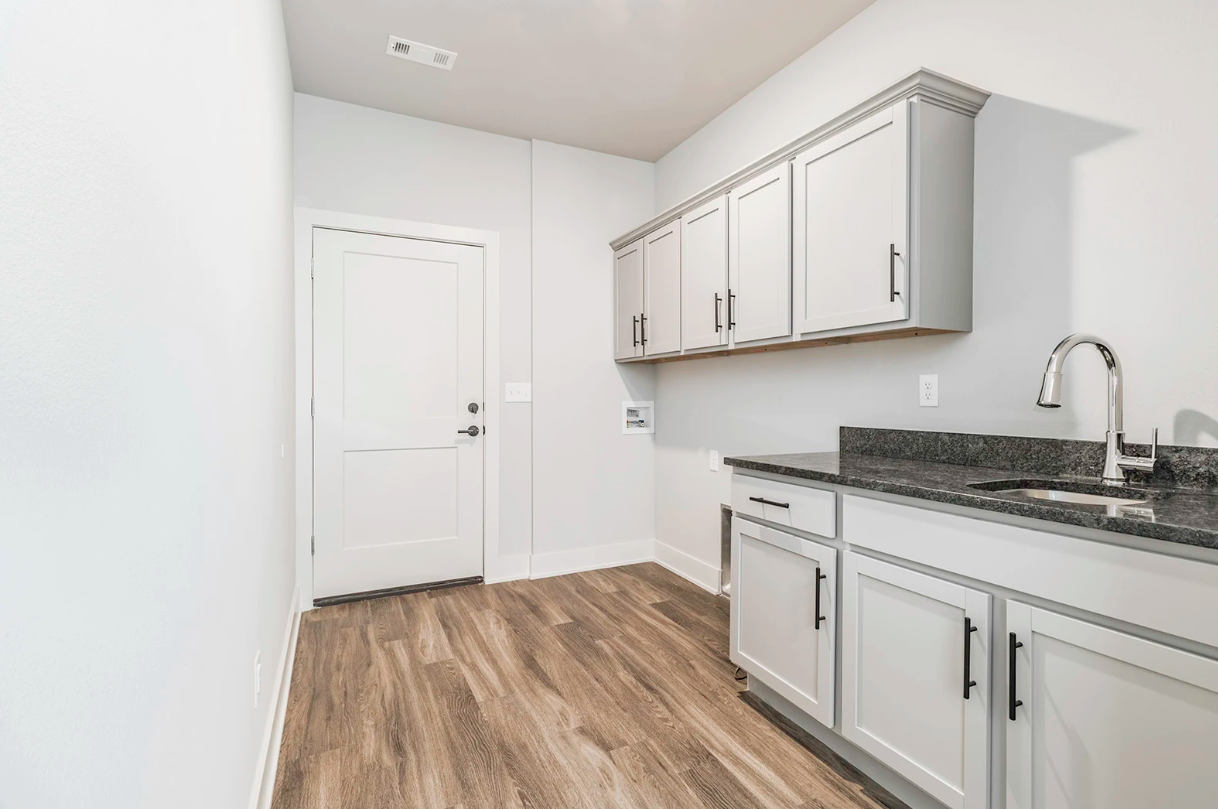 Laundry room with white cabinets, dark countertop, and wood-look flooring.