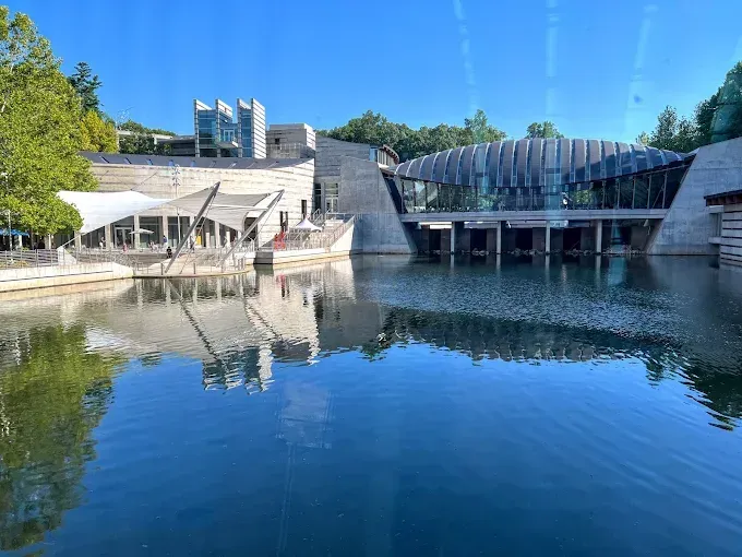 Modern building complex with reflective pool. Blue sky, water, and architecture with glass and stone.