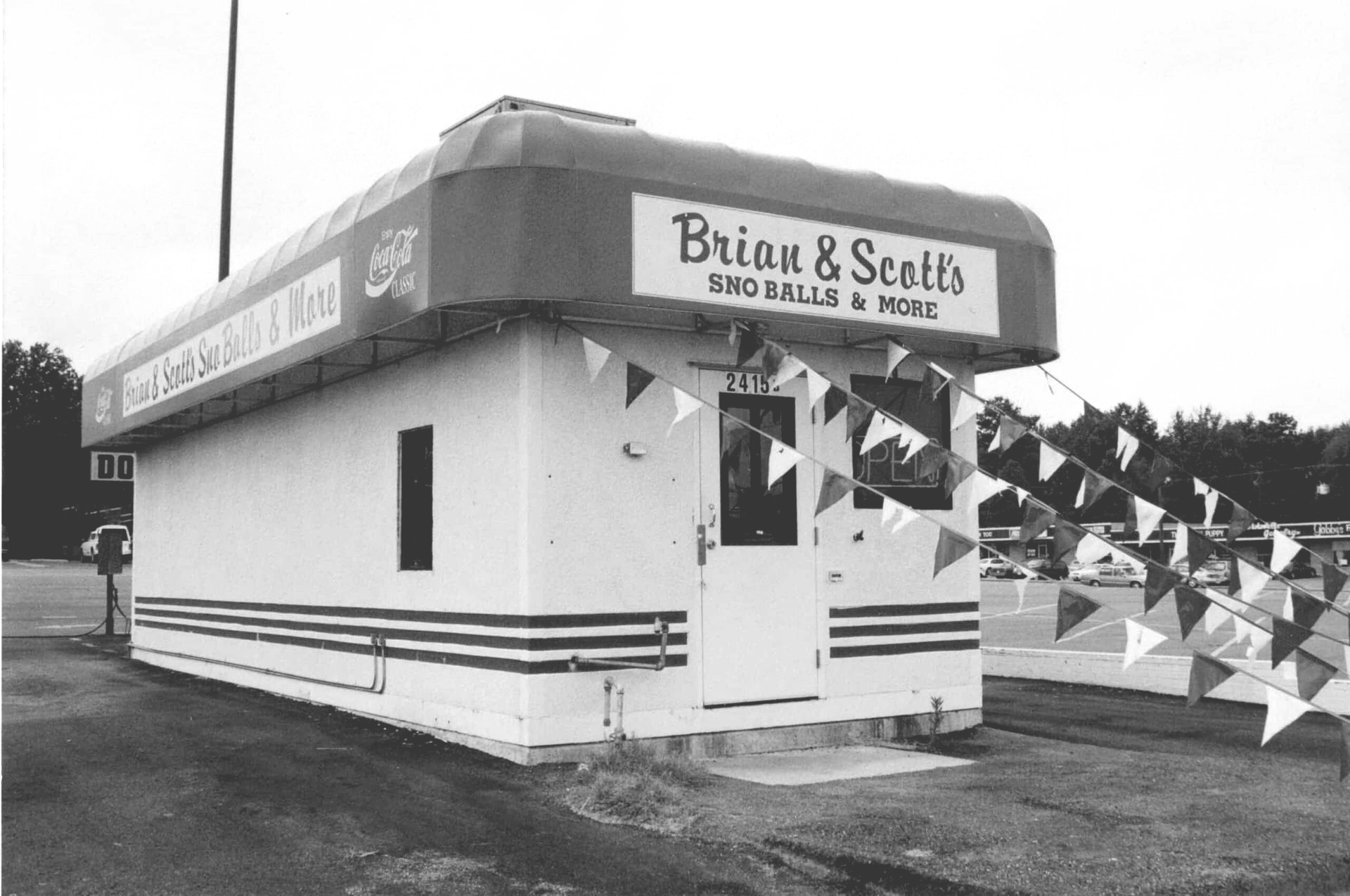 Small white-and-red Briou & Sclle shop with blue pennant flags outside on an overcast day