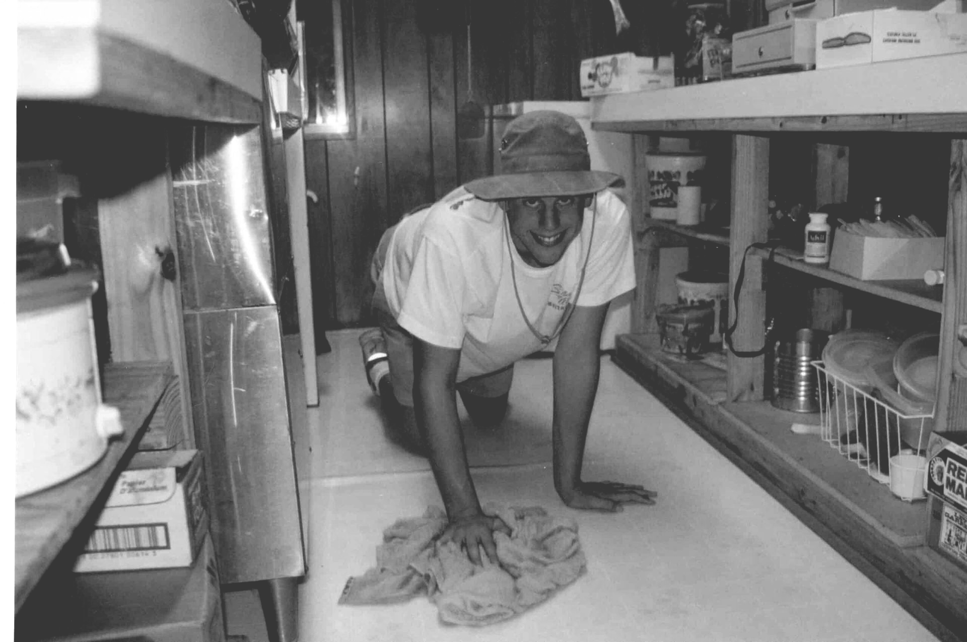 Person kneels on a kitchen floor, cleaning up a spill in a wooden pantry-style room.