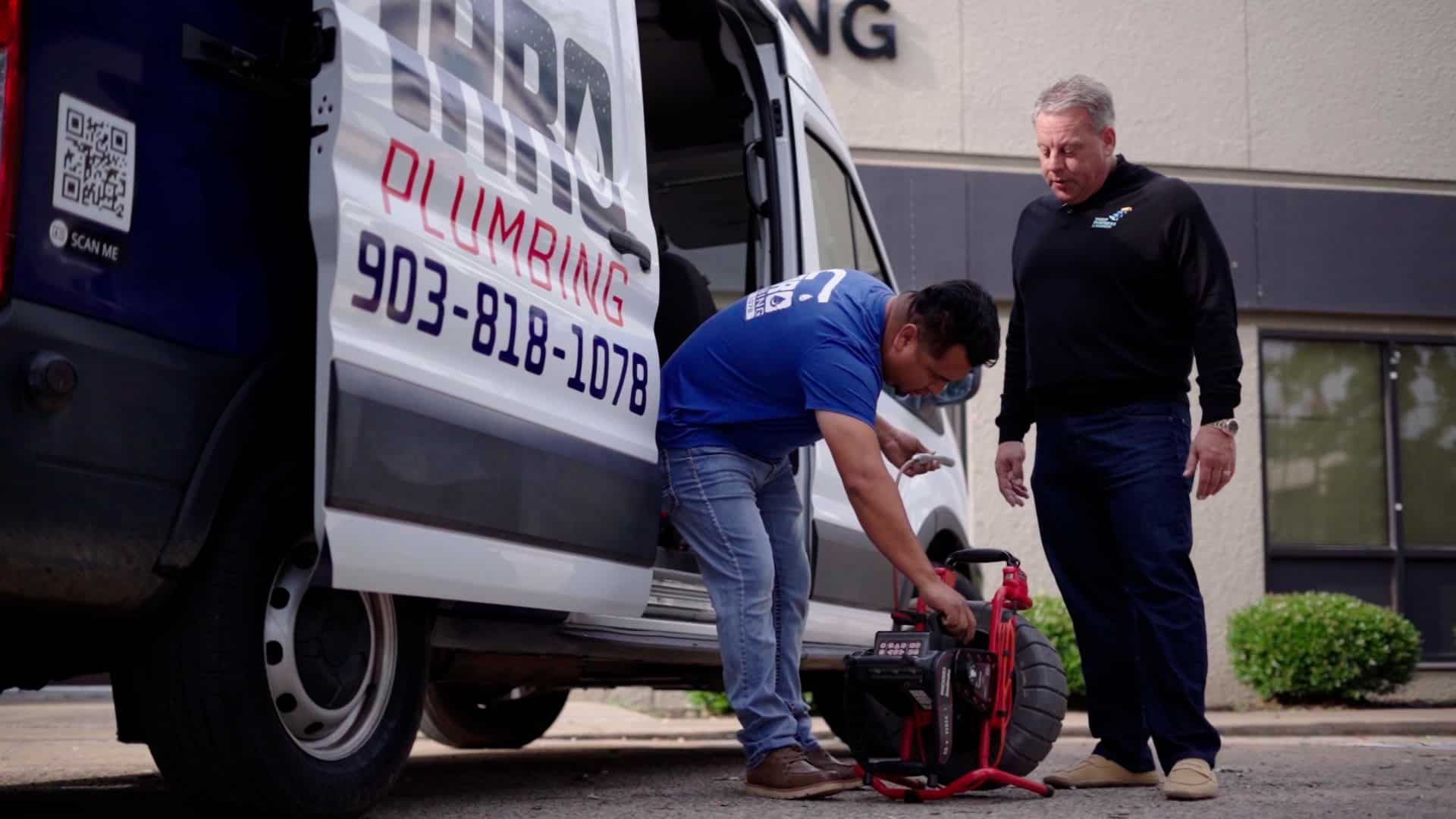 Two people fixing a red cable reel beside a white service van outside a building