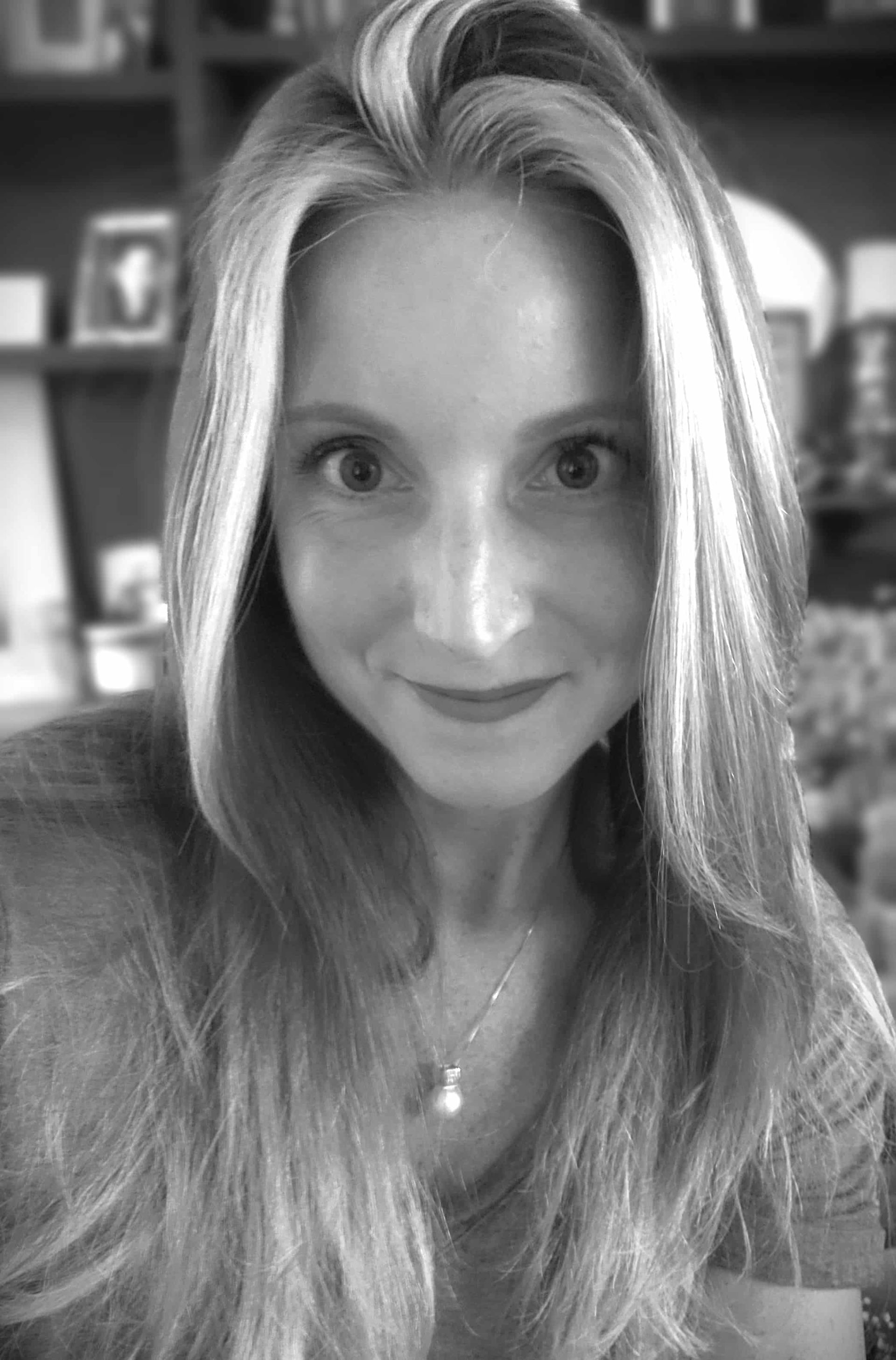 A woman with long blonde hair is smiling in a black and white photo.