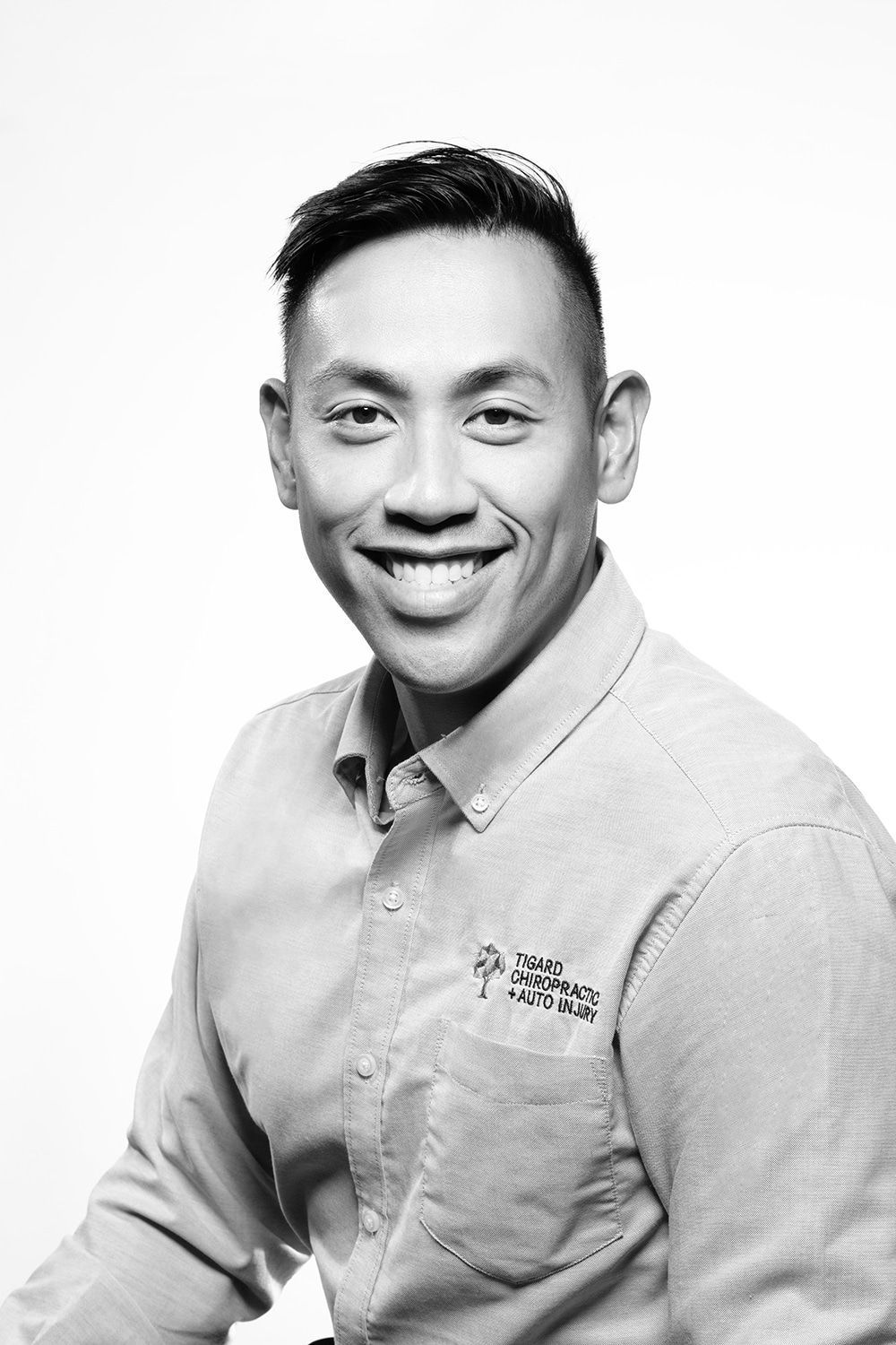 A black and white photo of a smiling man wearing a shirt. Tigard Chiropractic Team Photo.