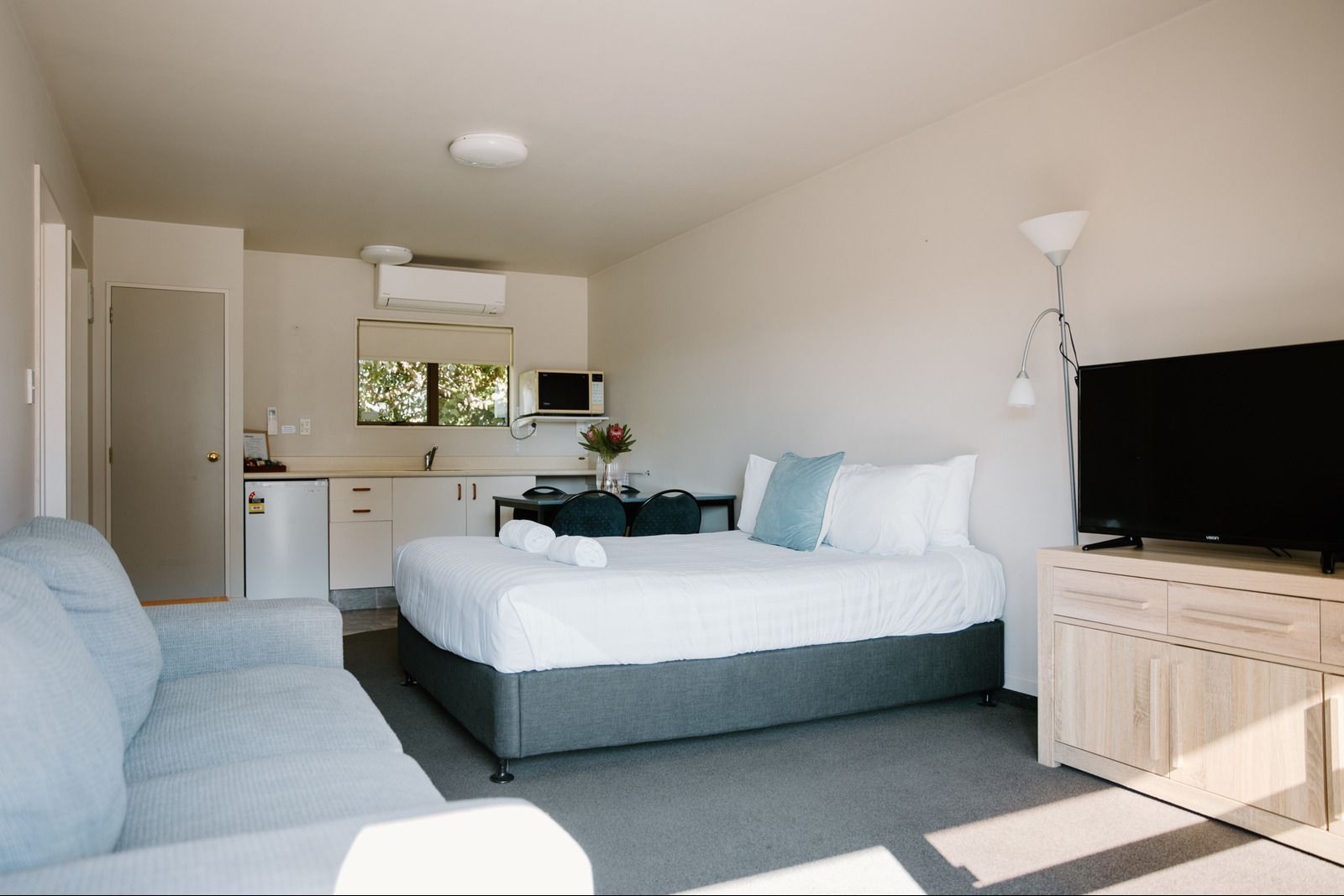 A Hotel Room With A Bed, Chair, Table And Microwave — Ambercourt Motel in Nelson, NZ