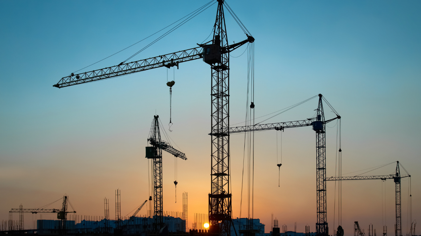 Construction cranes silhouetted against a colorful sunset.