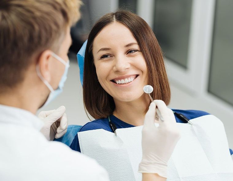 Dentist examining a smiling patient with a mirror in a bright clinic
