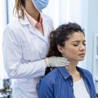Health professional wearing gloves examines a seated patient’s neck in a clinic