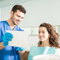 Dental staff showing a tablet to a smiling patient in a clinic room