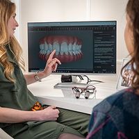 Two people review 3D teeth models on a computer in a dental consultation office.