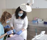 Dentist and assistant wearing masks treating a patient under a dental lamp
