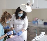 Dentist and assistant wearing masks treating a patient under a dental lamp